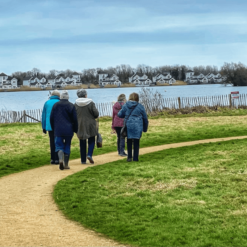 A group of people walking along the pathway by a lake in South Cerney