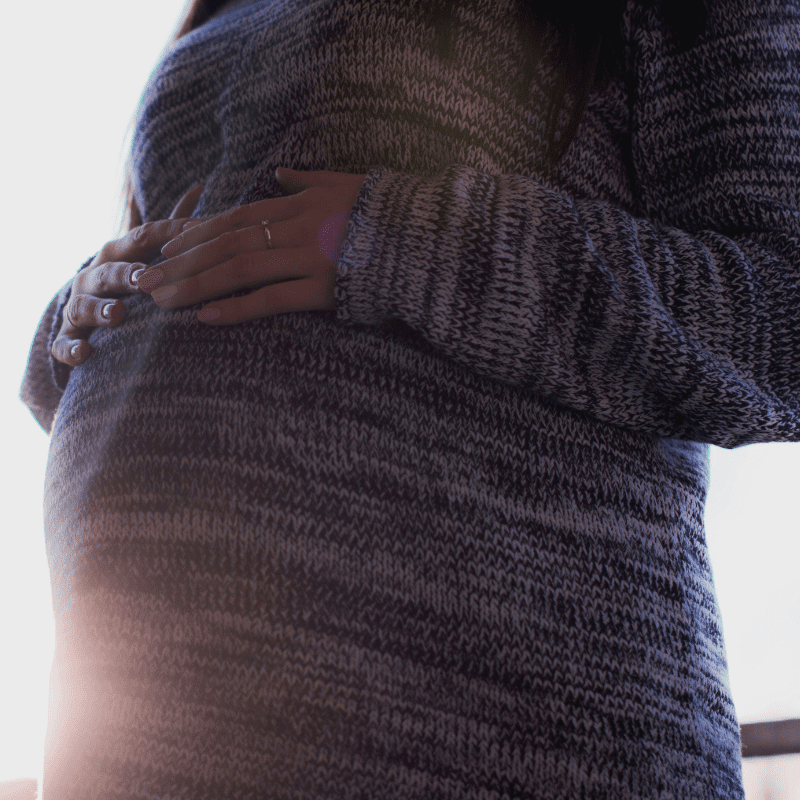 Image captures pregnant woman holding onto her pregnancy bump wearing a knitted jumper dress