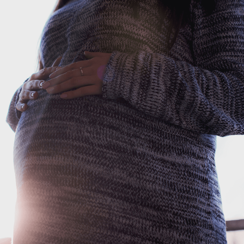 Ready Steady Baby Image captures pregnant woman holding onto her pregnancy bump wearing a knitted jumper dress